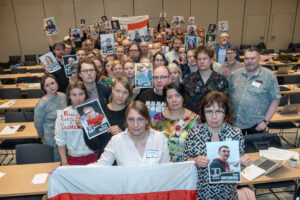Över 80 personer med allvarlig uppsyn håller i fotografier av personer. På fotona står namnet på personen samt ett årtal. Årtalet visar längden på fängelsedomen. I förgrunden finns Belarus flagga som hålls uppe av en person.